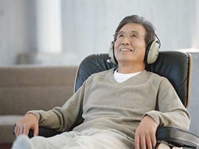 Senior man sitting on armchair wearing headphones, smiling